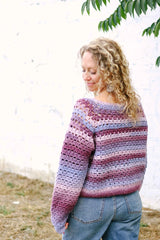 Back view of purple & pink crochet sweater worn by model with curly hair and blue jeans. thumbnail