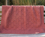 Full view of knit blanket with garter stitch border, draped over wooden bench. thumbnail