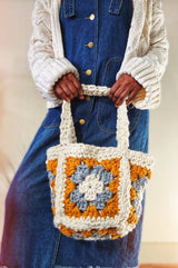 Woman in cream cardigan and denim dress holds smaller granny square bag in cream, mustard, and grey. thumbnail