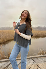 Woman stands on wooden dock in wetland area. She's turned to the side so you can see the split hem on the capelet. thumbnail