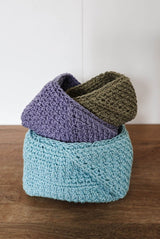 Three crochet baskets sitting inside each other at angles. They are on a dark wooden countertop with a white background. thumbnail