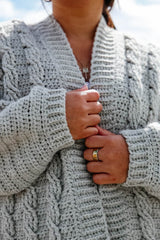 Close up of front of cardigan, showing ribbed front bands and crochet front panels. The sleeves are wide and have a ribbed cuff. thumbnail