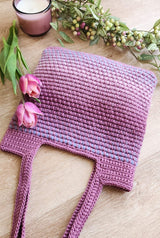 Crochet tote bag with shoulder-length straps is laid with straps facing viewer. An unlit candle and flowers frame the bottom of the bag. thumbnail