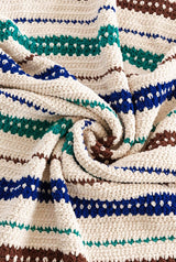 Close up of crochet blanket. It's made in cream with stripes of varying widths in green, royal blue, and chocolate brown. thumbnail