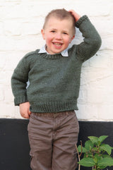 Young boy wears a green sweater over a collared shirt and brown pants. thumbnail
