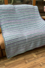 Crochet blanket in sky blue, greens, and purples draped over tan loveseat. thumbnail