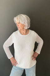 Front view of woman wearing a knit white long sleeve tee and pale jeans. thumbnail