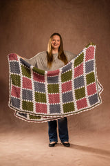 Woman standing in front of studio background holding crochet afghan folded in half. thumbnail