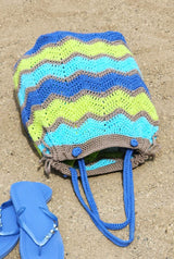 Crochet ripple bag laid flat on beach, with blue flip flops nearby. thumbnail