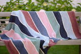 Full view of striped knit blanket draped over park bench. It is knot in stockinette stitch with ribbed borders. thumbnail