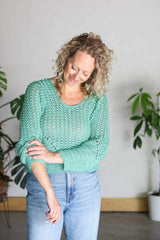 Front view of woman wearing crochet top with jeans, pushing up her right sleeve. The pullover has a scoop neck, a lace body, and solid hem & sides. thumbnail