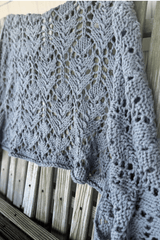 Close up of knit shawl draped over a worn wooden fence. thumbnail