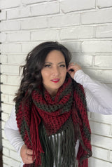 Woman leans against white painted brick wall with large knit shawl wrapped bandana style. thumbnail