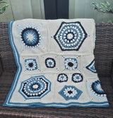 Crochet afghan laid over wicker outdoor couch, showing varied block sizes and striped border. thumbnail