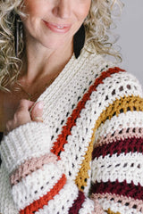 Close up of left shoulder and cuff, with model's arm raised, showing texture in crochet body and ribbed front band and sleeve hem. thumbnail
