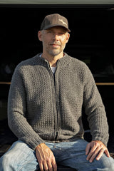 Man sitting, wearing grey crochet cardigan zipped to neck. thumbnail