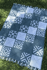 Top down view of crochet blanket laid flat on grass. The blanket has solid squares and patterned squares in 4 motifs. thumbnail
