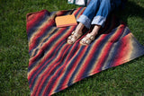 someone sitting on a multicolor afghan on the grass with a book thumbnail