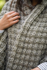 close-up of textured grey waffle-stitch knit blanket wrap with a striped sleeve visible thumbnail