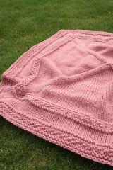 Pink knit blanket laid out on grass. thumbnail