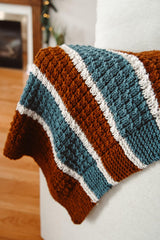 Brown, ivory, and teal striped blanket on cream couch. thumbnail