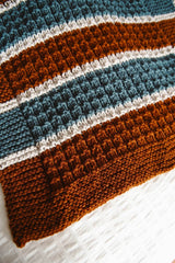 Close up on border of brown, ivory, and teal blanket. thumbnail