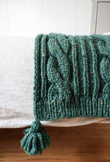 Close up of green blanket hem, with large cable, ribbing and tassel. thumbnail