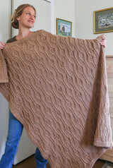 Woman holds tan crochet blanket, covering her from shoulder to ankle. thumbnail