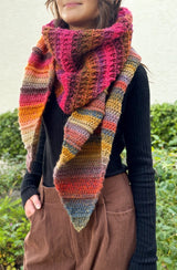 Woman wears a multi-textured and multi-color shawl in front of a bushy green background. thumbnail