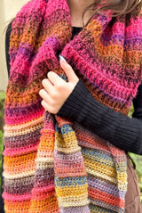 Close up of crochet shawl with blocks of pink-orange and multi-colored textured sections. thumbnail