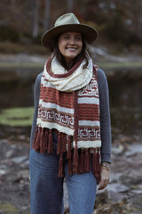 Woman wears cream, red, rust shawl wrapped around neck, standing in front of water.  thumbnail