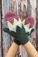 Close up of mittens in pink, cream, and green, modeled in front of weathered barn door.  thumbnail