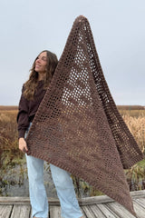 Woman holding brown mesh lattice afghan diagonally in front of body, on boardwalk.  thumbnail