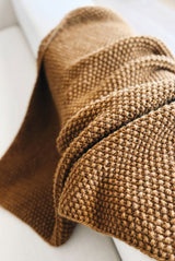 Close up of knit throw draped over the arm of a cream couch. The blanket is in a warm yellow brown and is knit in seed stitch for all over texture. thumbnail