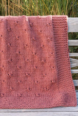 Medium pink knit afghan draped over park bench.  thumbnail