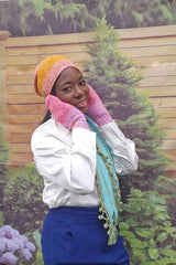 Woman in white top and blue skirt wears crochet beanie, matching mittens, and scarf with bobbled edge and tassels.  thumbnail
