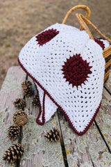 Crochet blanket folded in wicker basket, sitting on wooden picnic table with a collection of pinecones.  thumbnail