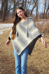 Woman stands in yard with brown grass and a bit of snow, wearing a crochet poncho in a self-striping grey and white yarn.  thumbnail