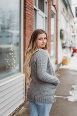 Back side view of woman wearing crochet cardigan on snowy small town sidewalk. The drop shoulder construction and shoulder seam is visible.  thumbnail
