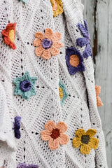 Close up of 3D crochet flowers of various types, in multi-colors, on a white crochet blanket.  thumbnail