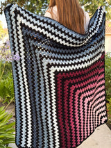 Mitered square crochet blanket held by woman standing outside on patio.  thumbnail
