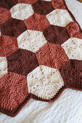 Crochet blanket with hexagon motifs in cream, warm tan, and chocolate brown. It's laid on a white duvet.  thumbnail