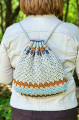 Crochet string backpack worn by woman in cream jacket. The bag is smaller than her back, cinched at the top.  thumbnail