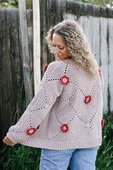 Back view of crochet cardigan worn over jeans. The cardigan body is a warm grey, with rust and pink flowers at the center of some squares.  thumbnail
