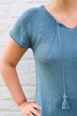 Close up of front of knit top, showing increase lines, split collar, and tassel trim.  thumbnail