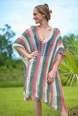 Woman wears a crochet poncho coverup in vertical stripes of cream, bright sage, and terracotta pink. The poncho has fringe along the lower edge.  thumbnail