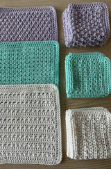 Set of three dishcloth patterns, with one cloth open on the left side and the other two folded and tacked. The cloths are shown in cream, aqua, and lilac.  thumbnail