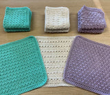 Three dishcloths arrayed in a semi-circle, with three stacks line up behind them. Each cloth has a different textured stitch pattern.  thumbnail