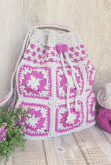 Crochet bag standing up on wooden plank table, filled and with top cinched.  thumbnail