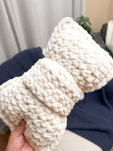 Close up of crochet bow pillow held above armchair.  thumbnail